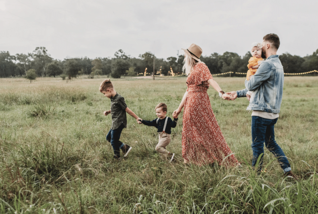 Family of 5 walking through a field holding hands.