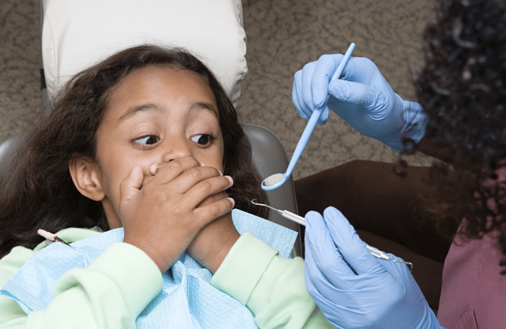 A dentist holding dental instruments and a girl covering her mouth with her hands.
