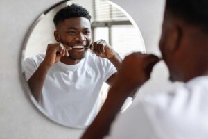 a teen flosses his teeth in the mirror