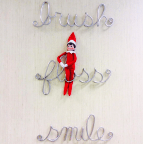 Wire signs say "brush floss smile". A stuffed toy elf is stuck in the word "floss".