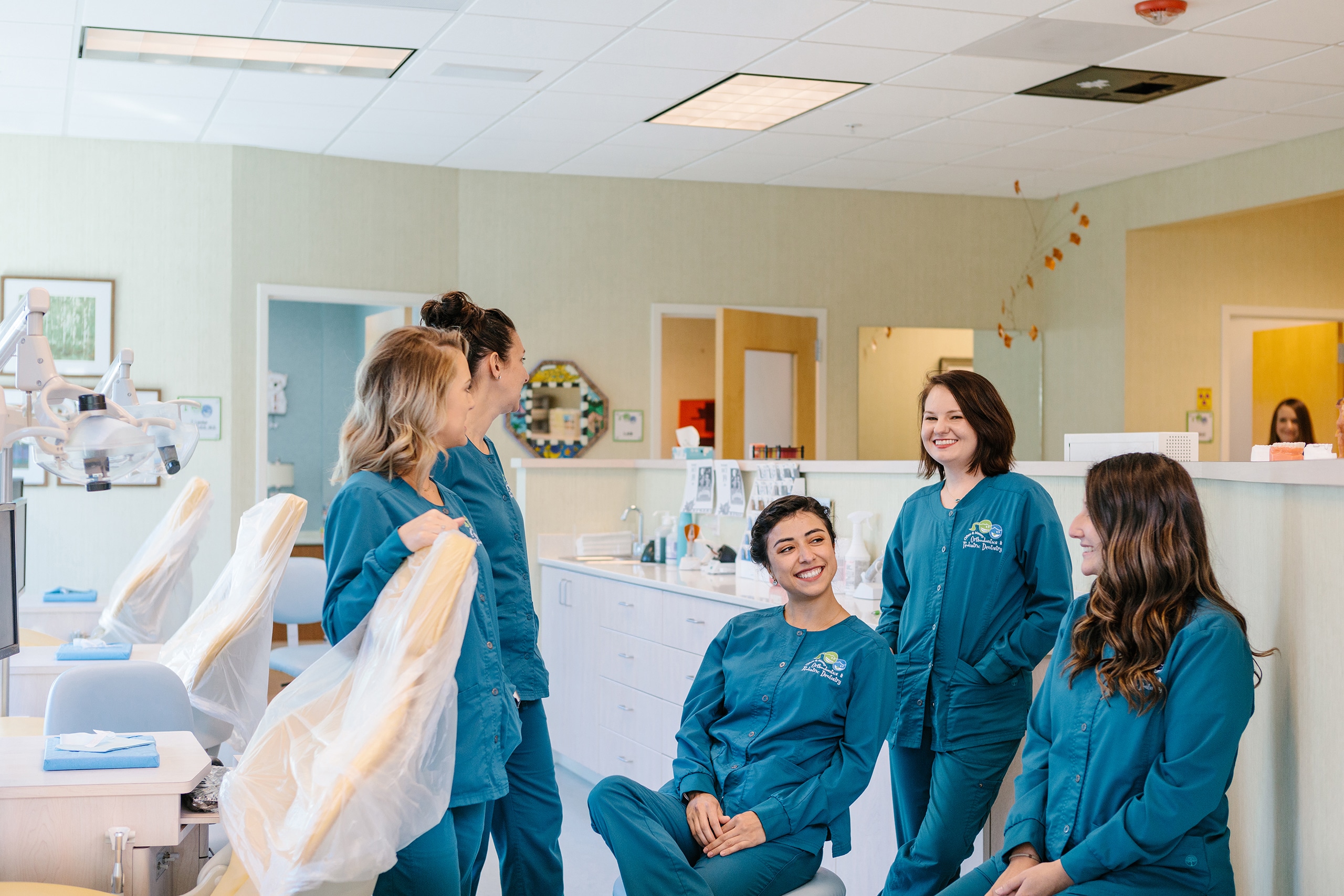 Four nurses in blue scrubs chatting in an exam room.