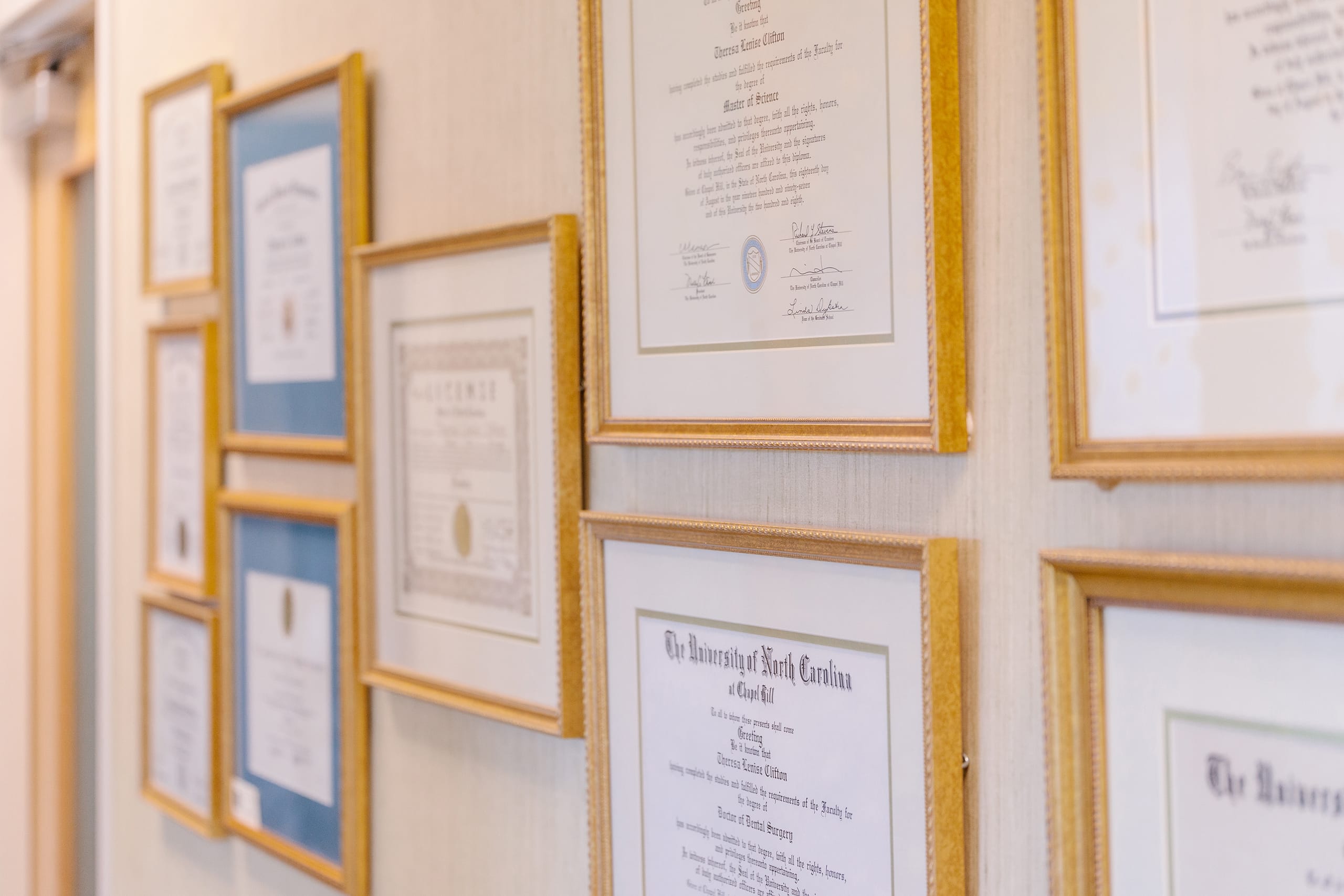A picture of a wall of framed certificates and degrees.