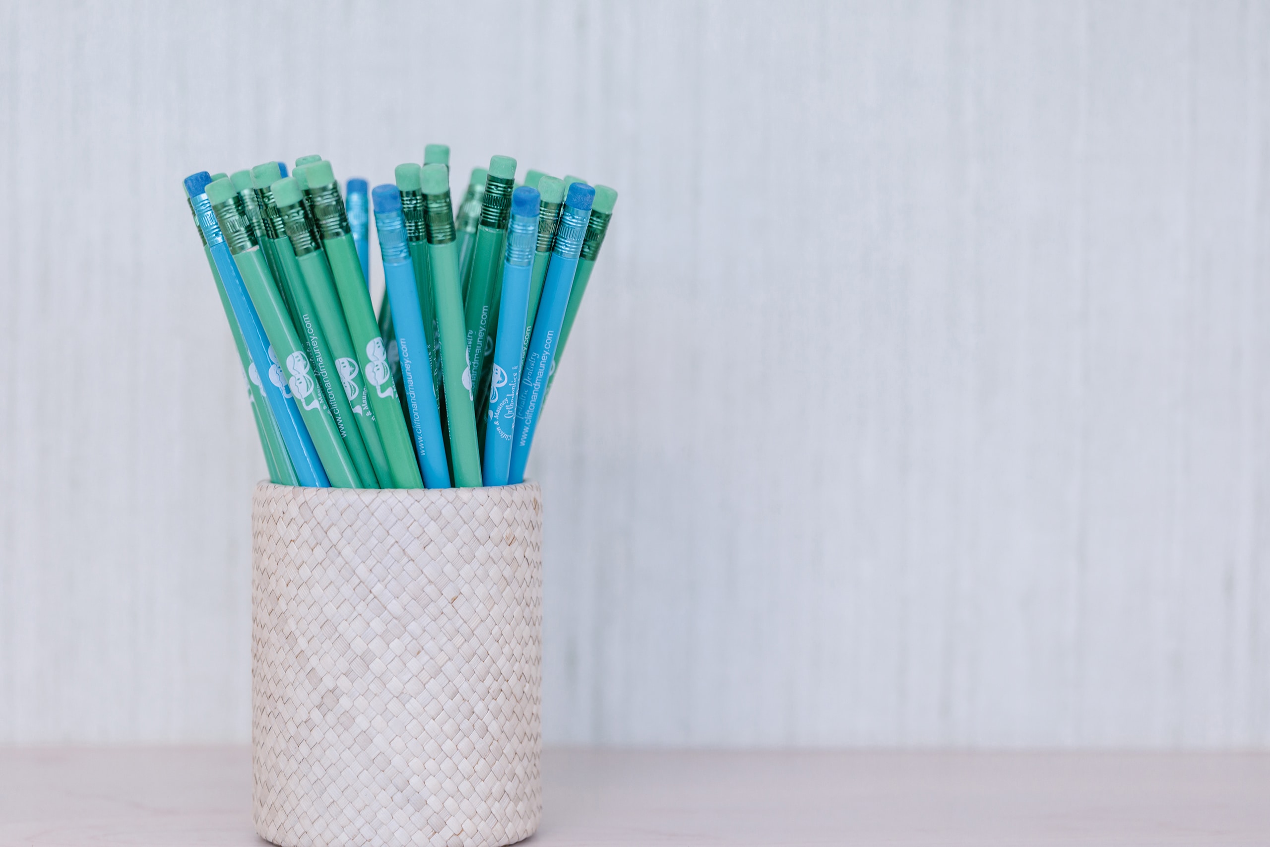 A woven pencil case filled with blue and green pencils.