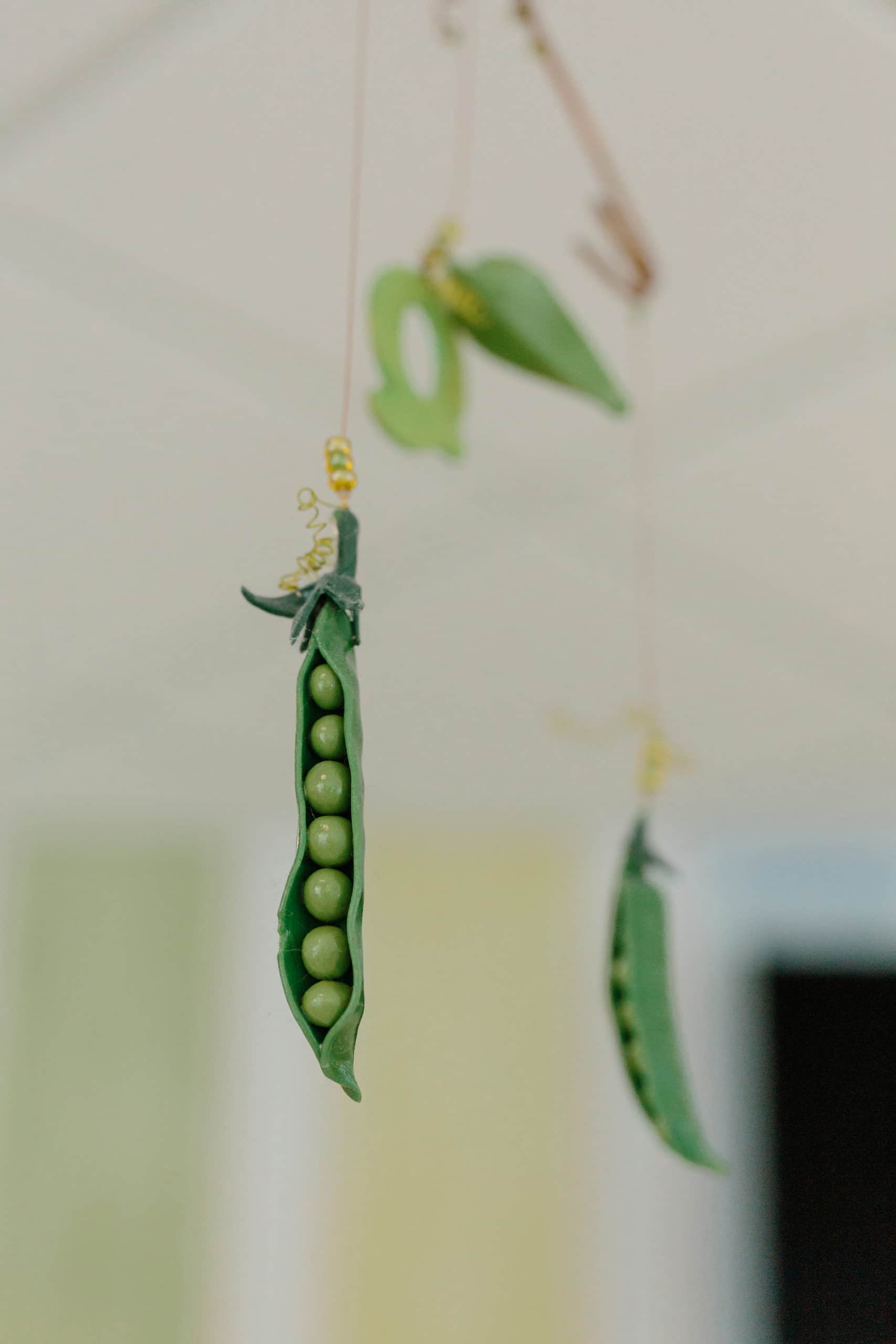 A close up of a ceiling mobile. Fake pea pods are hanging from its strings/
