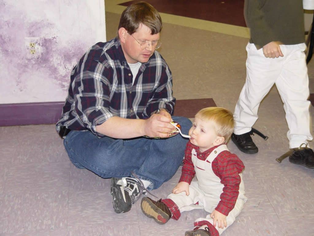 dr. chuck feeding his son while they sit on the floor in 2002