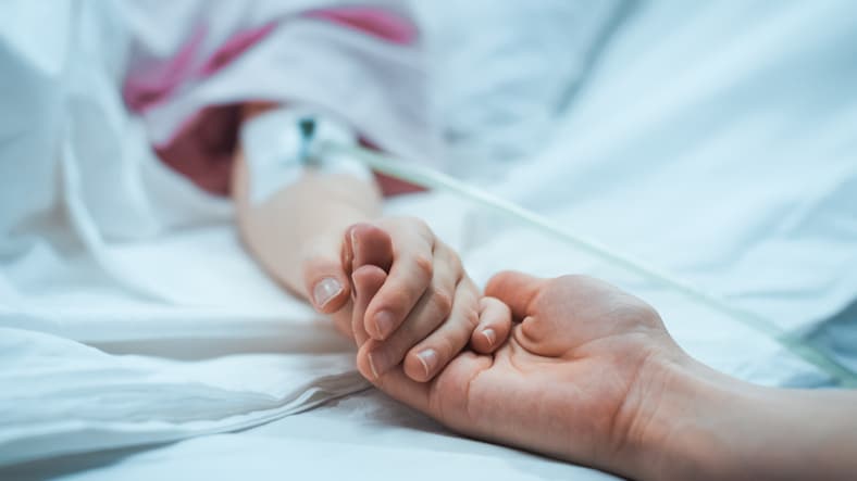 a parent holding the hand of a patient who is laying on a medical bed