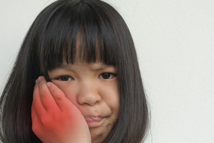 a little girl holding her cheek to express dental discomfort