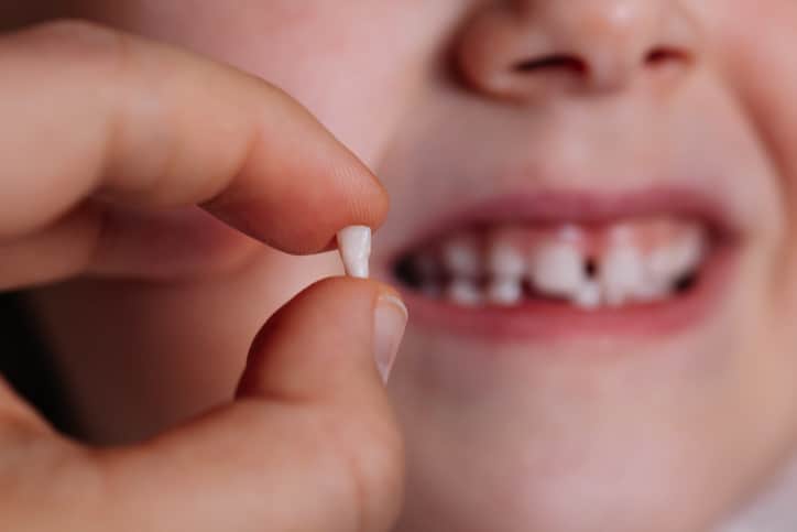 a young child holding up the baby tooth that they lost