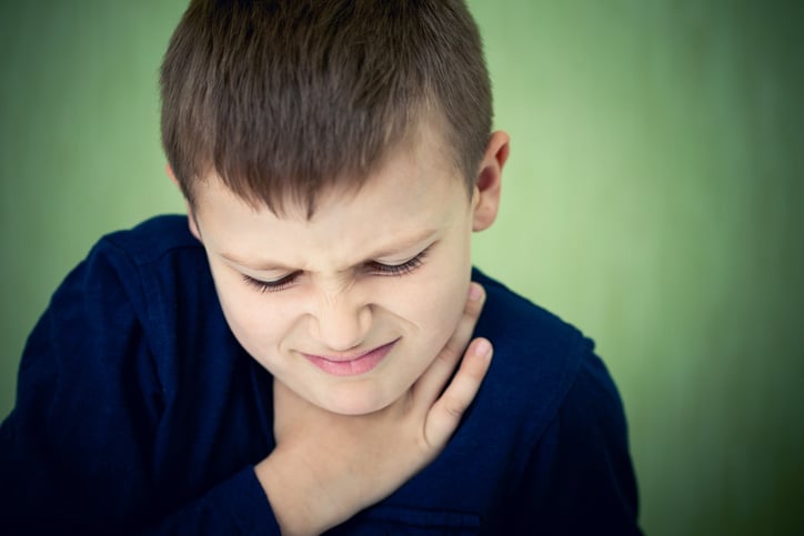 a young boy holding his neck to show signs of discomfort