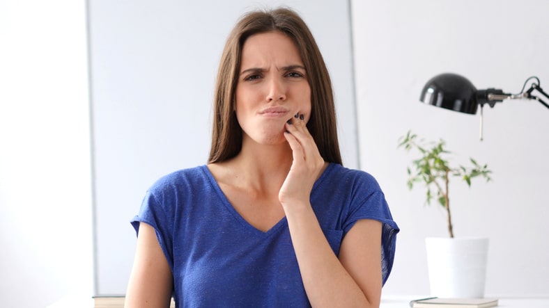a woman with a purple shirt holding her cheek to express dental discomfort