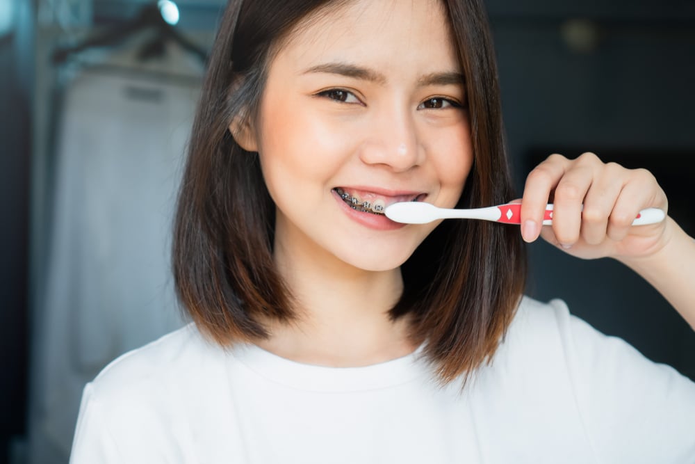 a teenage girl with metal braces brushing her teeth with a toothbrush