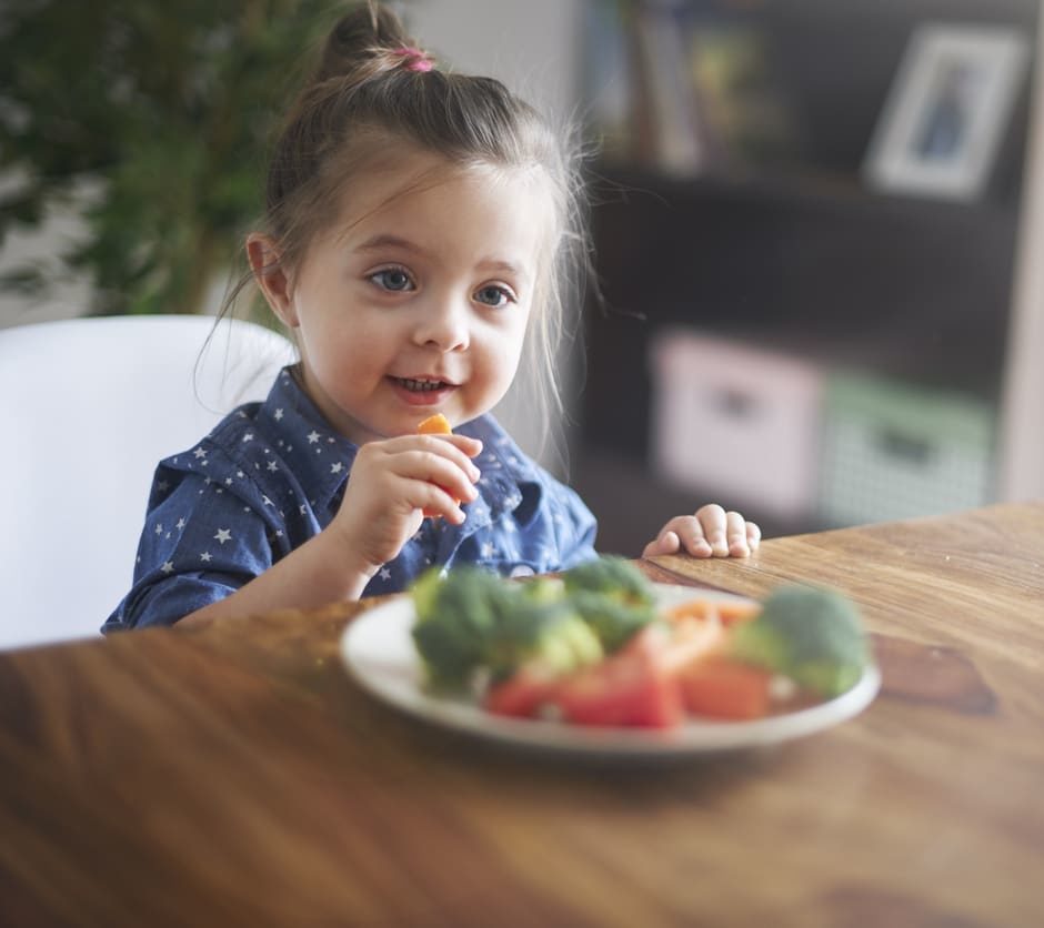 little girl sitting at the dinner table eating a bowl of veggies