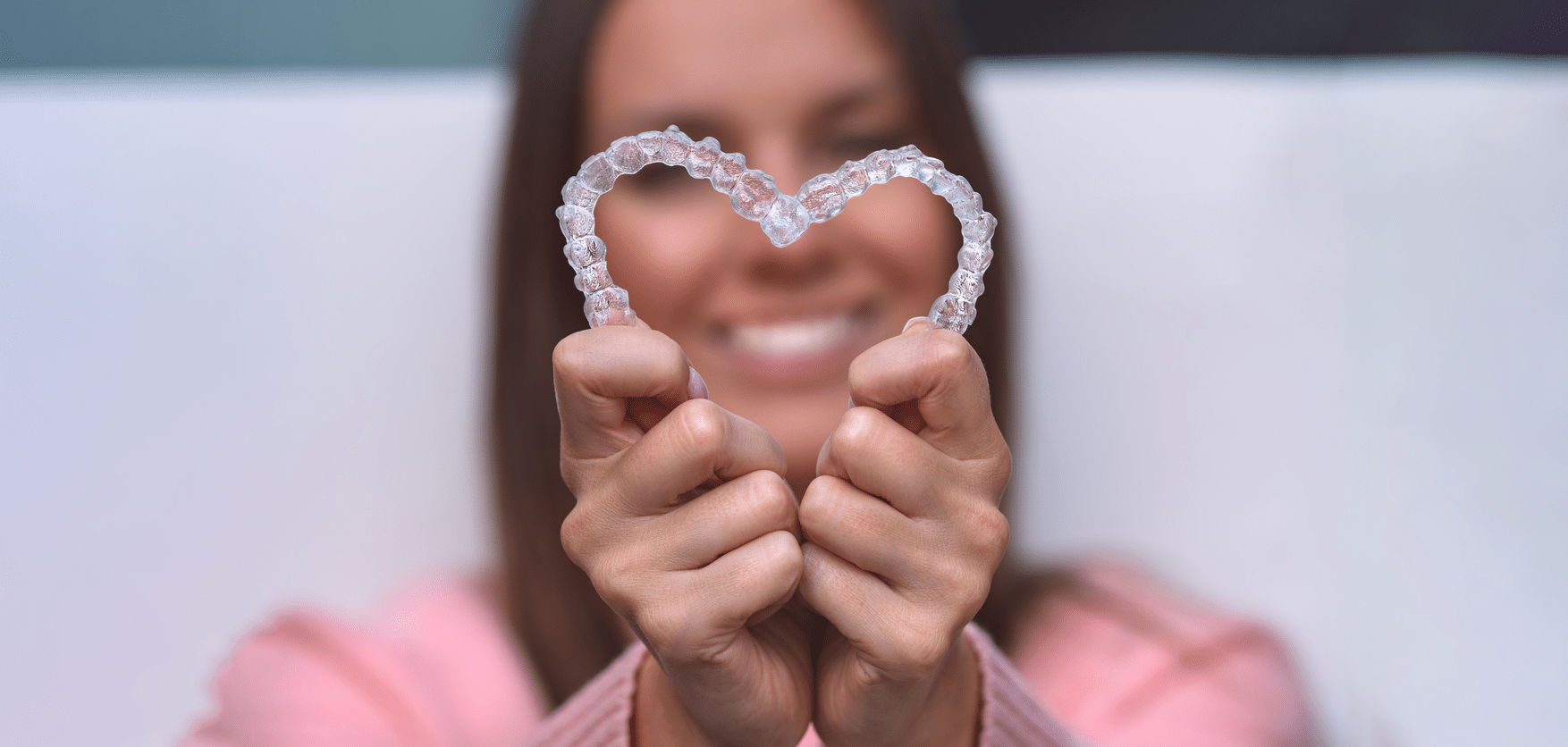 a woman holding up two invisalign aligners in the shape of a heart