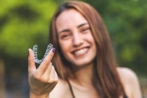 a smiling teen holds up her invisalign retainer
