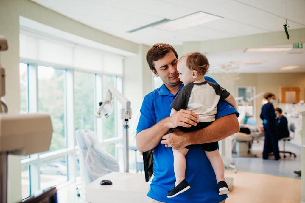 Young child at one of their first pediatric dental appointments. You can see that the office around this father and son has been designed with child psychology in mind.