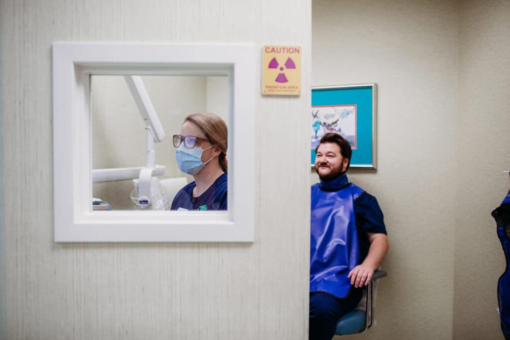 Two assistants in our x-ray room, one is pulling up records, the other is sitting for an x-ray.