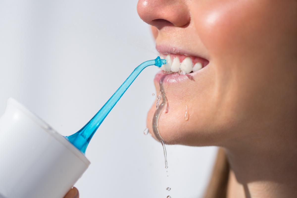 a woman uses a waterpik after brushing her teeth