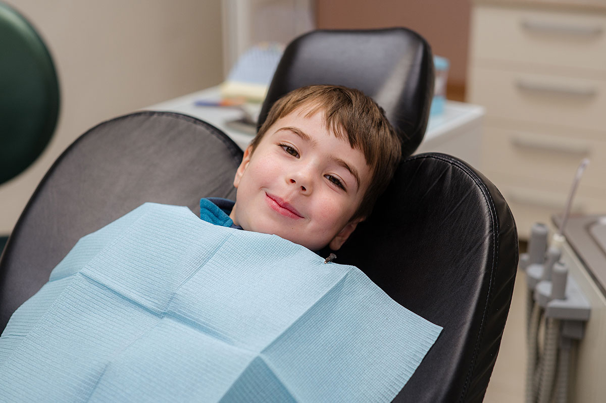 a child smiles in the dentist chair after receiving care for a pediatric dental emergency