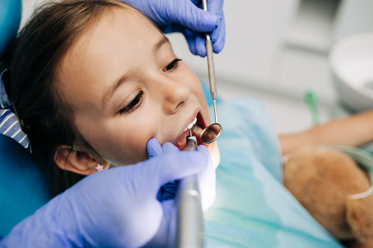 A young girl receives a dental checkup as a dentist uses tools to examine her teeth.